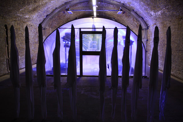 Tamsyn Challenger. Monoculture, 2013. Polytunnel, soil, OSR, blue led grow lights, zentai suits, embroidery silks. Installation view, Beaconsfield, Vauxhall.