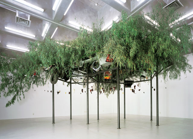Chen Zhen. Fu Dao/Fu Dao, Upside-Down Buddha/Arrival at Good Fortune, 1997. Steel, bamboo, resin Buddha statues, washing machine, computer monitor, tires, bicycle, fan, chair, household appliances, other found objects, and string, approximately 350 x 800 x 550 cm overall. Courtesy Galleria Continua, San Gimignano/Beijing/Les Moulins/Havana.