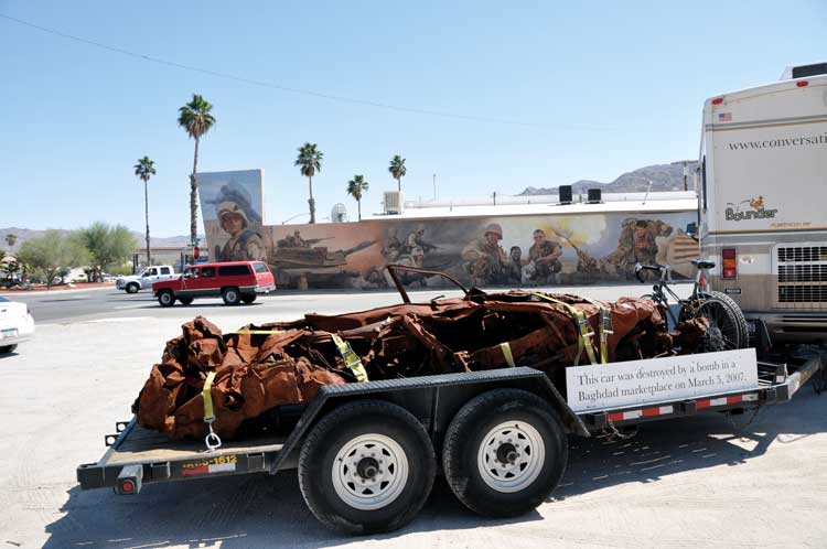 Jeremy Deller. It Is What It Is, 2009. The car in front of a mural depicting the fall of Baghdad near 29 Palms, California. Courtesy of The Artist and The Modern Institute / Toby Webster Ltd., Glasgow.