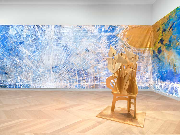 Thomas Houseago. Foreground: My Studio Chair & Flowers, 2024. Brass, 66⅜ × 37⁷⁄₁₆ × 32¹¹⁄₁₆ in (168.6 × 95.1 × 83 cm); Background: Sunrise, 2024. Acrylic and oil on canvas, 120 × 1364 in (304.8 × 3464.6 cm). Image courtesy of Lévy Gorvy Dayan gallery.