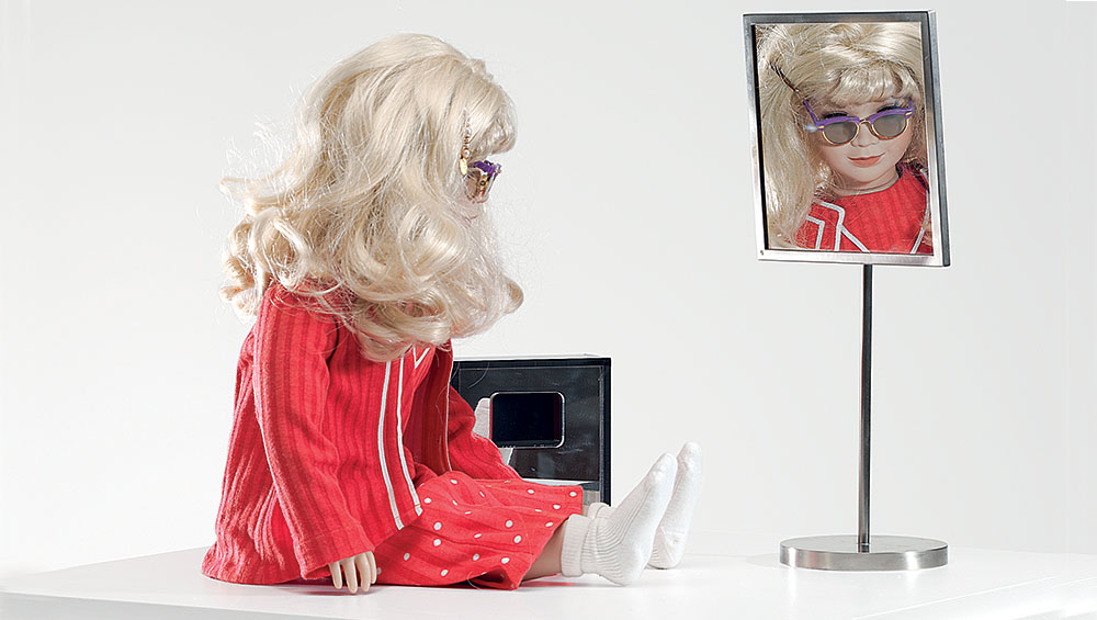 Lynn Hershman Leeson. CyberRoberta, 1996. Custom-made doll, clothing, glasses, webcam, surveillance camera, mirror, original programming, and telerobotic head-rotating system, approximately 17 ¾ x 17 ¾ x 7 ⅞ in (45 x 45 x 20 cm). Courtesy the artist; Bridget Donahue Gallery, New York; and Altman Siegel, San Francisco.