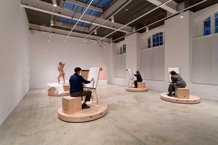 Laura Lima, The Drawing Drawing, 2026. Mechanised platforms (wood, metal, motors, electrical components, wheels), life model, paper, pencils and pens, still life display, ICA visitors. Installation view, Institute of Contemporary Arts, London. Photo: Anne Tetzlaff.