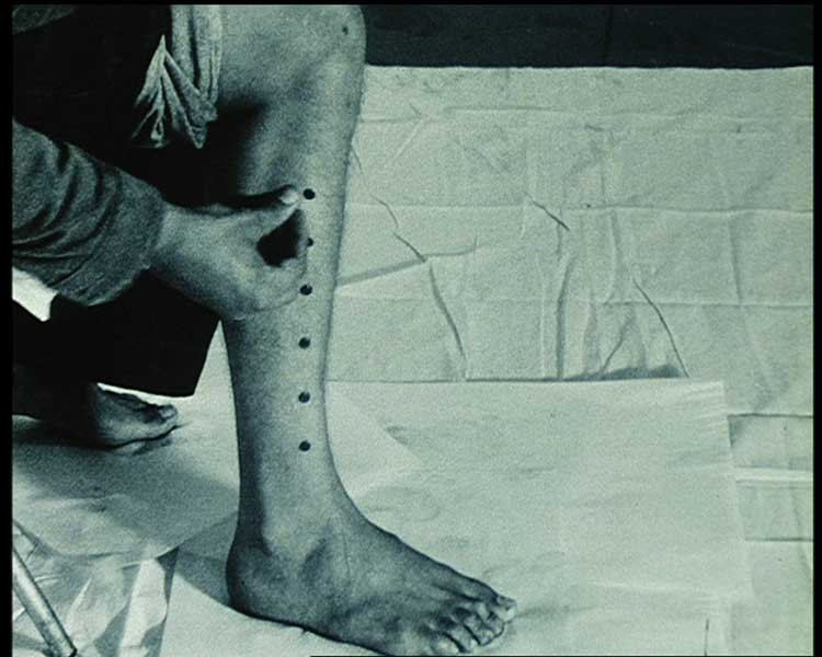 Mike Parr. Push tacks into your leg until a line of tacks is made up your leg (Wound by Measurement). Performed at Galerie Impact, Lausanne, Switzerland, 1973. 16mm film still.