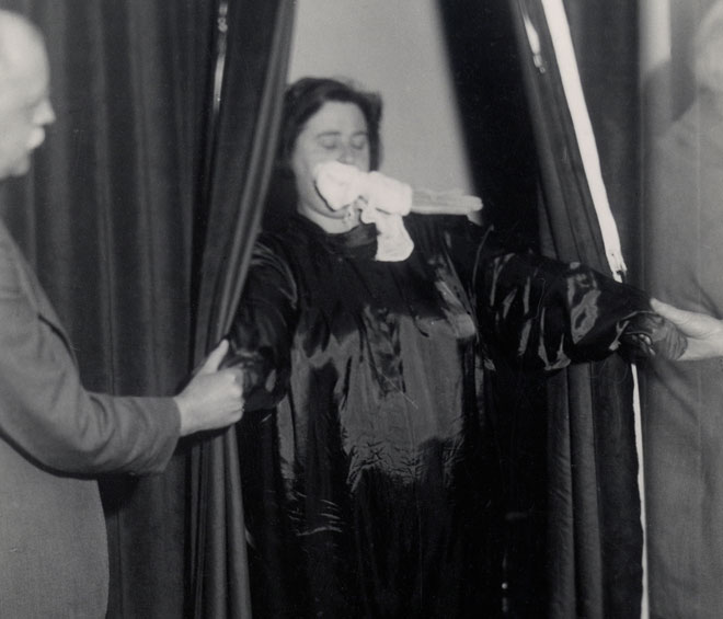 Helen Duncan emerging from curtains with ‘ectoplasm’ – her hands holding those of others
at the séance, Edinburgh, 1933. Photograph © Senate House Library, University of London.